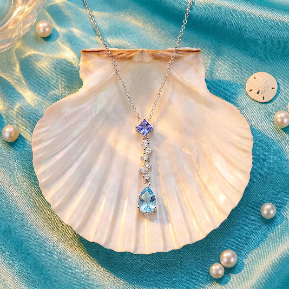 The Ocean Tear necklace inside a pearly scallop shell on turquoise silk