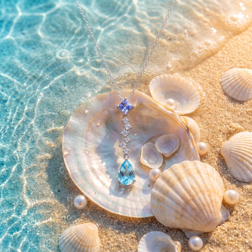 The “Ariel” Ocean Tear Necklace resting on pearly seashells in shallow turquoise water