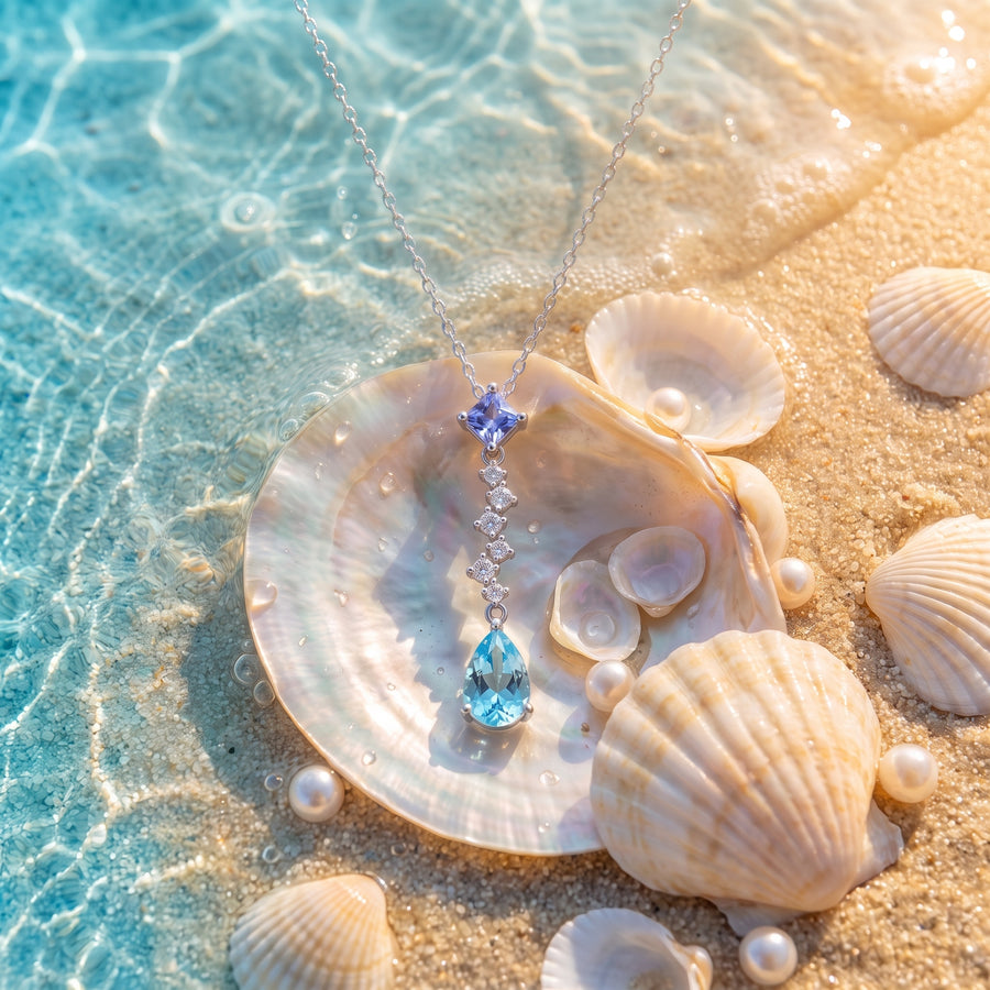 The “Ariel” Ocean Tear Necklace resting on pearly seashells in shallow turquoise water