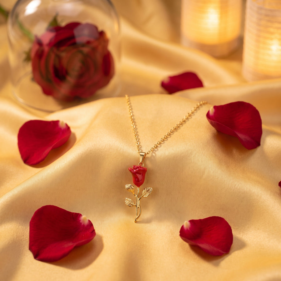 The “Belle” Enchanted Rose Necklace resting on golden satin with red rose petals
